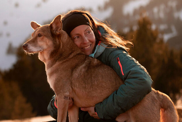Frau umarmt seitlich stehenden großen Hund mit hellbraunem Fell