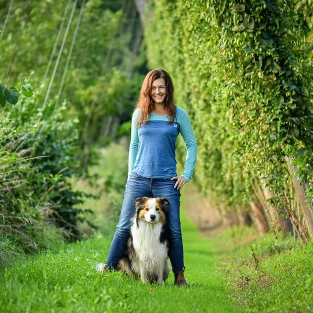 Frau steht in der Natur hinter einem Hund