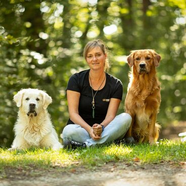 Frau sitzt zwischen zwei Hunden in der Natur
